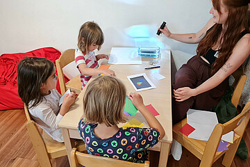 Drei Kinder und eine Erzieherin sitzen an einem Tisch und führen Experimente durch.