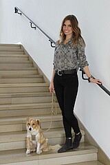 Auf dem Bild ist eine Studentin mit ihrem Hund zu sehen. Sie steht auf Treppenstufen.